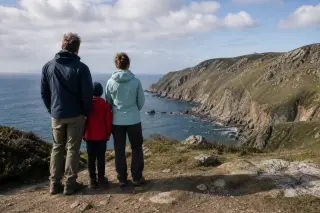 A family wearing outdoor gear enjoys a scenic coastal view from a safe viewpoint above the cliffs of Cap de la Hague under a partly cloudy sky.