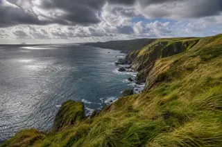 Cliffs of the Cotentin Peninsula at La Hague with windswept grass, dramatic clouds, and sunlight breaking through over the sea