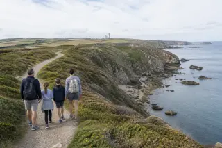 Coastal cliffs and grassy land of La Hague with a family walking on a path near the sea under a cloudy sky