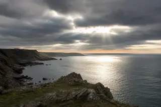 Falaises du Cotentin illuminées par un rayon de soleil sous un ciel nuageux, vue panoramique sur la côte et la mer avec des jeux de contraste lumineux