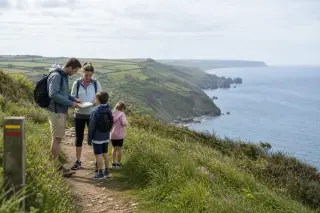 Famille de randonneurs en pause sur un sentier balisé au sommet d'une falaise verdoyante du Cotentin, vue sur la mer, ambiance naturelle et calme