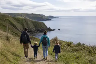 Famille marchant sur un sentier côtier des falaises de la Hague, par temps calme, avec vue sur la mer et lumière douce.