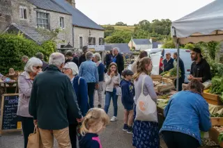 Village market scene in Normandy with people of all ages mingling near rustic stalls, bathed in gentle daylight.