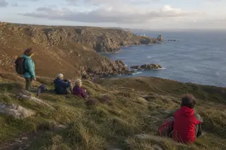 Group of hikers pausing on Cap de la Hague cliff, gazing at the coastline in soft natural evening light, candid and immersive atmosphere