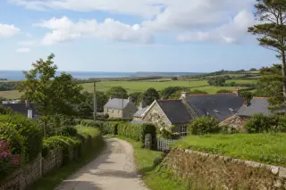 Hameau de Branville-Hague avec maisons en pierre, jardins et vue sur la mer sous un ciel nuageux