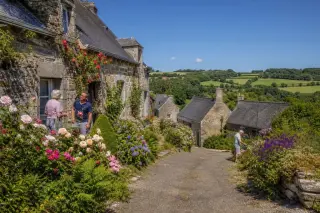 hameau rural français avec maisons en pierre, jardins fleuris, quelques habitants, chemins entretenus, sous une lumière d'été
