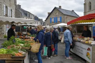 Marché local en plein air dans un village normand avec des étals de produits frais et une ambiance conviviale sous un ciel nuageux.