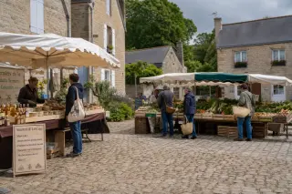 Marché local en plein air dans un village normand, avec quelques visiteurs et producteurs, stands de produits artisanaux sous une lumière douce, dans une ambiance conviviale.
