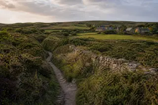 paysage bocager de la Hague, lande, muret de pierres sèches, chemin creux, hameau en arrière-plan sous un ciel nuageux
