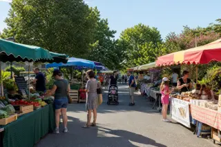 Scène de marché en plein air en été, avec stands de produits locaux, familles et acheteurs sous une lumière naturelle, ambiance conviviale.