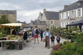 scène réelle d’un marché de village printanier, habitants circulant entre les étals sur une place entourée de maisons en pierre