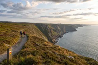 Sentier balisé sur les falaises du cap de la Hague avec deux randonneurs, paysage naturel et lumineux, mer en arrière-plan.